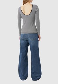 Gestreiftes Langarmoberteil mit tiefem Rückenausschnitt und schwarzem Saum, kombiniert mit weit geschnittenen blauen Jeans. Beide Kleidungsstücke haben eine legere Passform.