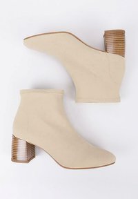 Botas de tobillo beige hechas de tela texturizada con un tacón de bloque. El tacón presenta rayas verticales, lo que realza el interés visual del diseño.