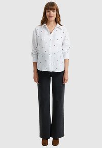 White button-up shirt with small black heart patterns, features a chest pocket. Paired with dark, wide-leg jeans and brown ankle boots.