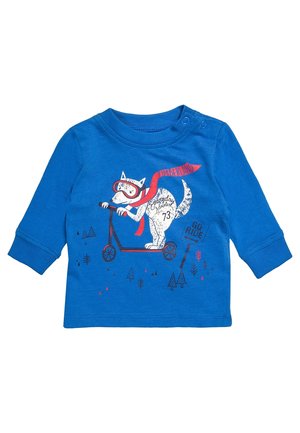 Niebieska koszulka z długim rękawem dla malucha, z białym psem w goglach i czerwonym szaliku, jadącym na hulajnodze obok znaku "Jedź dalej" oraz małych drzewek.