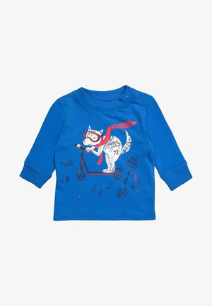Camiseta azul de manga larga para niño pequeño con un perro blanco que lleva gafas y una bufanda roja, montando un patinete junto a un cartel que dice "Go Ride" y pequeños árboles.
