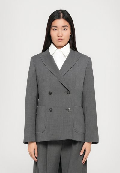 Grå dobbelbrystet blazer lavet af struktureret stof, med to frontlommer, sorte knapper og en krave med spids over en hvid skjorte.