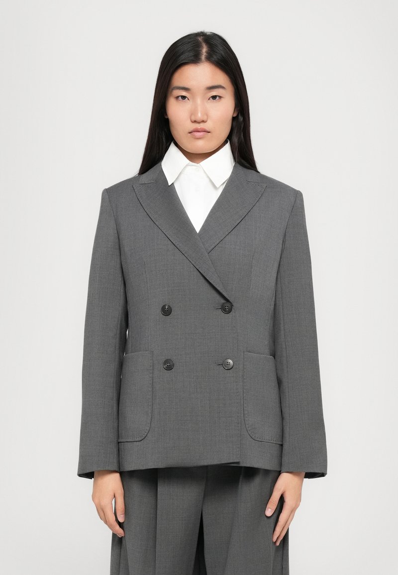 Blazer grigio doppiopetto realizzato in tessuto testurizzato, con due tasche frontali, bottoni neri e colletto a rever sopra una camicia bianca.