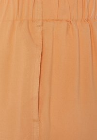 Detailní záběr na broskvovou látku s nařaseným elastickým pasem a s vertikálním švem.