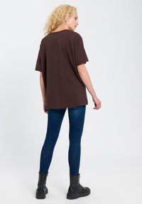 Brązowy, oversize t-shirt z krótkim r�ękawem, okrągłym dekoltem, połączony z ciemnoniebieskimi slim fit jeansami i czarnymi botkami za kostkę. Prosty design, bez wzorów.