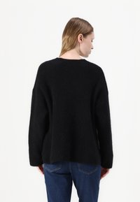 Pulover negru supradimensionat dintr-o textură pufoasă, cu un guler larg, umeri căzuți și o margine dreaptă, asortat cu blugi denim albaștri.
