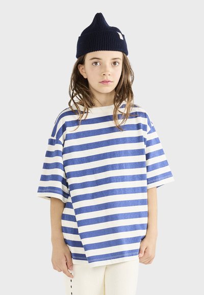 Stribet bomulds t-shirt med blå og creme horisontale striber, oversized pasform, korte ærmer, parret med en marineblå beanie-hat.
