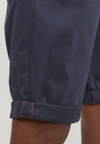 Pantaloni corti blu navy in cotone con una superficie liscia, dotati di risvolti cuciti con cuciture rosse per un tocco di dettaglio.