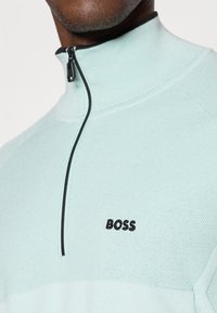 Ανοιχτό μπλε μισό φερμουάρ πουλόβερ κατασκευασμένο από υφασμένο ύφασμα. Διαθέτε�ι μαύρο φερμουάρ και κεντημένο λογότυπο "BOSS" στο στήθος.