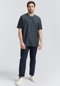 Donkergrijze korte mouwen henley shirt met een contrasterende kraag, gecombineerd met marineblauwe broek en witte sneakers. Eenvoudige textuur, relaxed fit.