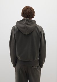 Felpa con cappuccio verde scuro, dal taglio morbido, con polsini e orlo a coste, realizzata in tessuto morbido, mostrata da dietro.