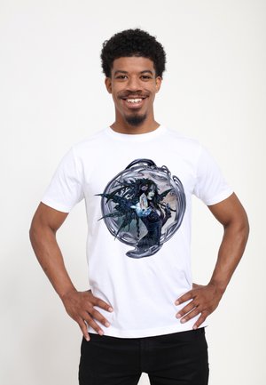 Homme souriant portant un t-shirt blanc présentant une illustration de dark fantasy d'une femme ailée tenant un objet lumineux dans un cadre circulaire orné.