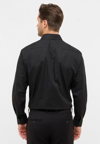 Camicia nera a righe con maniche lunghe, colletto e polsini con bottoni. Il tessuto è liscio con una leggera lucentezza e righe verticali.