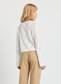 Pull blanc court avec motif en losanges, texture tricotée et manches larges, associé à un pantalon beige taille haute.