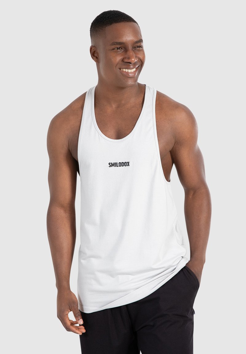 Weißes Tanktop mit runder Ausschnittform und ärmellosem Design. Mit schwarzem "SMILODOX"-Logo auf der Brust. Aus weichem, leichtem Stoff.