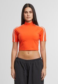 Lyhythihainen, korkeakauluksinen crop-top kirkkaassa oranssissa, venyvää materiaalia ja valkoisia sivuvasteita. Sileä pinta, tiukka malli.