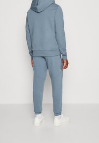 Felpa con cappuccio e pantaloni abbinati in tessuto azzurro chiaro. Texture morbida con polsini e vita elasticizzati. Sneakers bianche completano l'outfit.