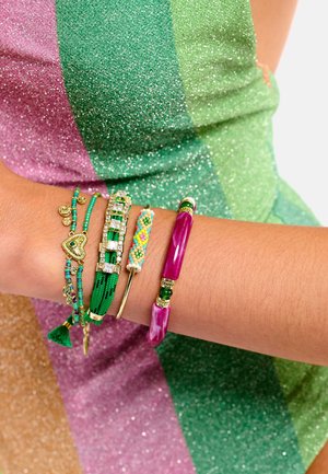 Bracelets colorés au poignet : fils verts, accents dorés, motif en perles, et un bracelet rigide rose brillant avec perles et détails verts.