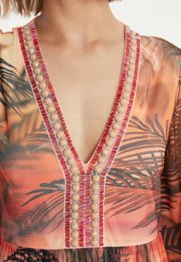 V-Ausschnittkleid mit tropischem Druck in Orange und Pink. Verfügt über dekorative Perlen und gestickte Akzente entlang des Ausschnitts und des Oberteils.