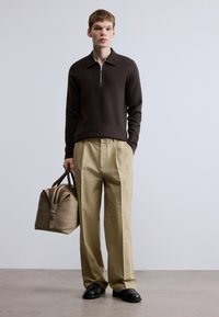 Καφέ πουλόβερ με φερμουάρ, μπεζ παντελόνι με ψηλή μέση και μαλακή, δομημένη μπεζ τσάντα με σκούρα στοιχεία. Λείες υφές και καθαρές γραμμές.