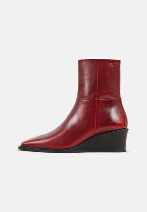 Red leather ankle boot with pointed toe and black wedge heel, side view on white background.