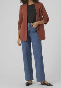 Rostfärgad blazer med trekvartsärmar, kombinerad med höga blå denimjeans. Svarta spetsiga ballerinas fulländar outfiten.