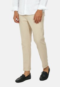 Pantaloni di cotone beige a taglio slim, con tasche frontali e orli arrotolati, abbinati a mocassini di pelle nera.