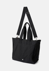 Μαύρη τσάντα tote με διπλές ανυψωτικές λαβές και ρυθμιζόμενο ιμάντα ώμου; κατασκευασμένη από ανθεκτικό ύφασμα; διαθέτει μια μινιμάλ λεπτομέρεια λογότυπου.