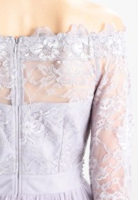 Levandulové šaty s off-the-shoulder krajkovým živůtkem s květinovými vzory, průhlednými rukávy a texturovaným zipem v pase.