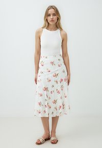 Weißer Spitzenrock mit floralem Druck in Pink und Grün, kombiniert mit einem enganliegenden weißen Tanktop und neutralen Sandalen.