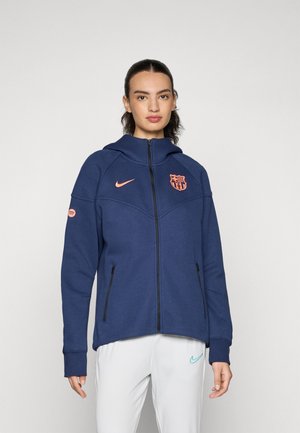 Marineblå genser med glidelås og høy krage, oransje logo og Barcelonas våpenskjold. Har sidelommer og ribbestrikkede mansjetter for komfort.