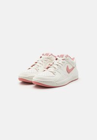 Les baskets Nike présentent une tige en cuir blanc avec des accents roses, un bout perforé, un laçage avant et une semelle en caoutchouc rose.