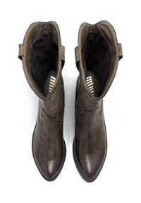 Botas de cuero marrón con punta afilada, costuras decorativas a lo largo de la parte superior y tiradores en los laterales para facilitar el uso. Suelas planas.