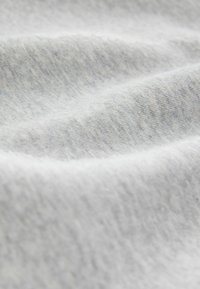 Tissu doux gris clair avec une texture tricotée lisse, montré en gros plan avec des plis délicats et des ombres subtiles.