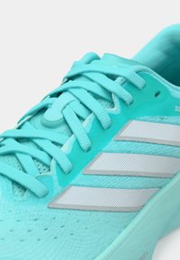 Τιρκουάζ αθλητικό παπούτσι με υφασμάτινη επιφάνεια, μαξιλαρωμένη γλώσσα και τρεις λευκές ρίγες στο πλάι. Οι κορδόνια είναι επίπεδα και ενσωματωμένα.