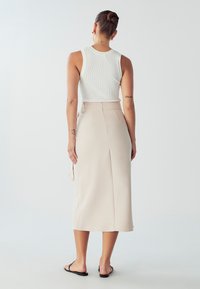 Lahka bež midi krila z gladko, tekočo teksturo in izpostavljenim zadrgo na hrbtni strani, v kombinaciji s prilega belim rebrastim topom.