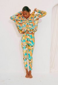 Kleurvolle trainingsoutfit bestaande uit een cropped jack en leggings. Gemaakt van een lichtgewicht materiaal, met levendige patronen in geel, blauw en groen.