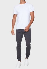 White cotton t-shirt paired with dark gray joggers. Joggers feature a tapered design with elastic cuffs and side seams. White sneakers complete the outfit.