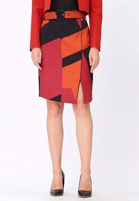 Jupe crayon multicolore présentant des motifs géométriques en rouge, orange et noir ; fente haute et détail de ceinture ; associée à des talons noirs.