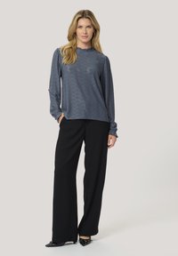 Top blu di cotone a maniche lunghe con scollo arricciato abbinato a pantaloni neri a gamba larga e scarpe nere a punta.