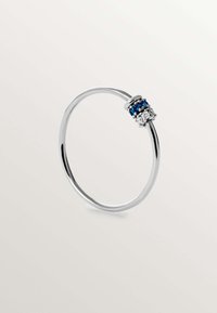 Anillo de plata con una banda delgada y un conjunto de piedras azules y transparentes en un acento circular. Textura suave, diseño minimalista.
