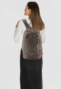 Mochila de cuero gris con cremalleras prominentes, superficie texturizada, correas acolchadas y forma redondeada, llevada en la espalda de una persona.