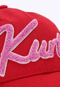 Cappellino rosso di cotone con testo ricamato in rilievo "Kurt" in rosa con contorno bianco. Texture liscia e forma strutturata.