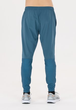 Blaue sportliche Jogginghosen aus leichtem Material, mit tailliertem Design und Mesh-Einsätzen an den Unterschenkeln. Graue Laufschuhe inbegriffen.