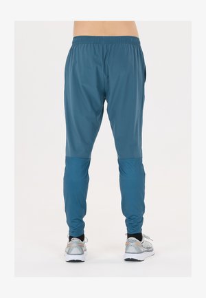 Blaue sportliche Jogginghosen aus leichtem Material, mit tailliertem Design und Mesh-Einsätzen an den Unterschenkeln. Graue Laufschuhe inbegriffen.