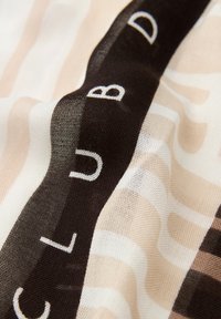 Gennemsigtigt tørklæde med bølgende beige, brune og cremefarvede mønstre. Indeholder kraftig sort tekst. Letvægtsstof med en glat tekstur.