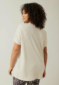 Lys beige top med en rynket tekstur, korte ærmer og en afslappet pasform, parret med leggins i leopardprint.
