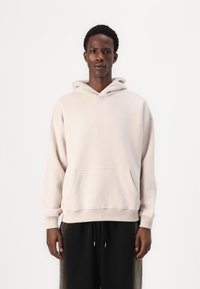 Lys beige hætte sweatshirt med en frontlomme og ribbede manchetter. Stoffet ser blødt ud, og den har en afslappet, løs pasform.