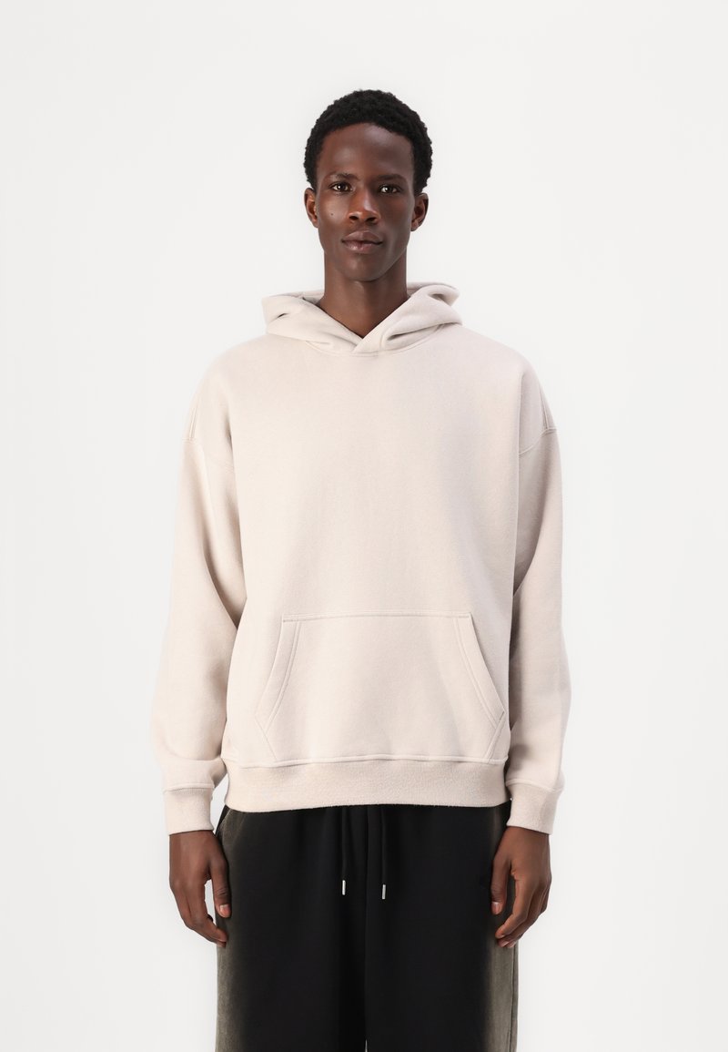 Lys beige hætte sweatshirt med en frontlomme og ribbede manchetter. Stoffet ser blødt ud, og den har en afslappet, løs pasform.