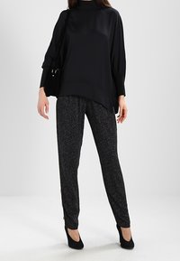 Czarna satynowa bluzka z długim rękawem i wysokim kołnierzem, zestawiona z czarnymi, wzorzystymi spodniami o dopasowanym kroju. Całość uzupełniają czarne szpilki.